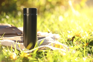 Photo of Black thermos and blanket on green grass outdoors, space for text