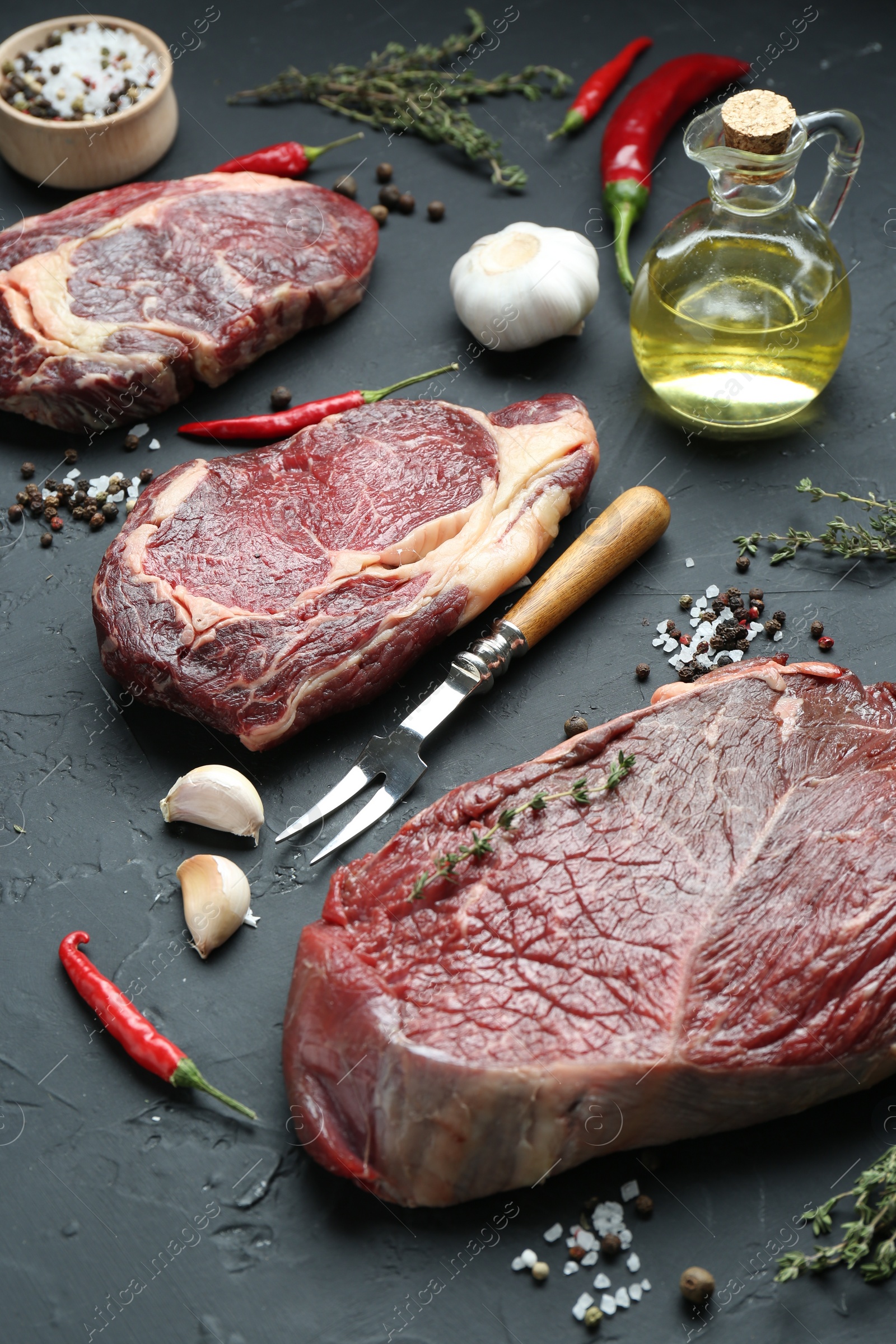 Photo of Pieces of raw beef meat, products and spices on dark grey textured table