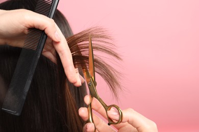 Photo of Hairdresser cutting client's hair with scissors on pink background, closeup. Space for text