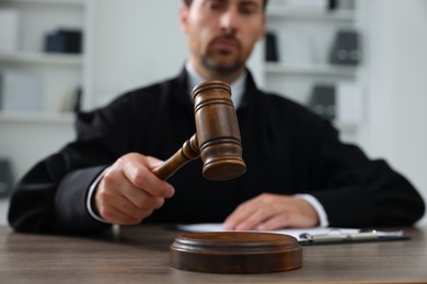 Judge with gavel and papers sitting at wooden table indoors, selective focus