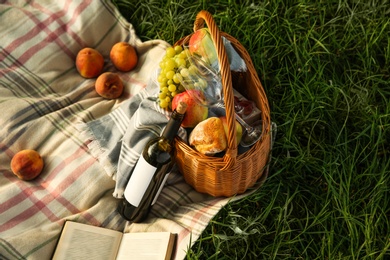 Photo of Picnic blanket with delicious food and wine on green grass, above view