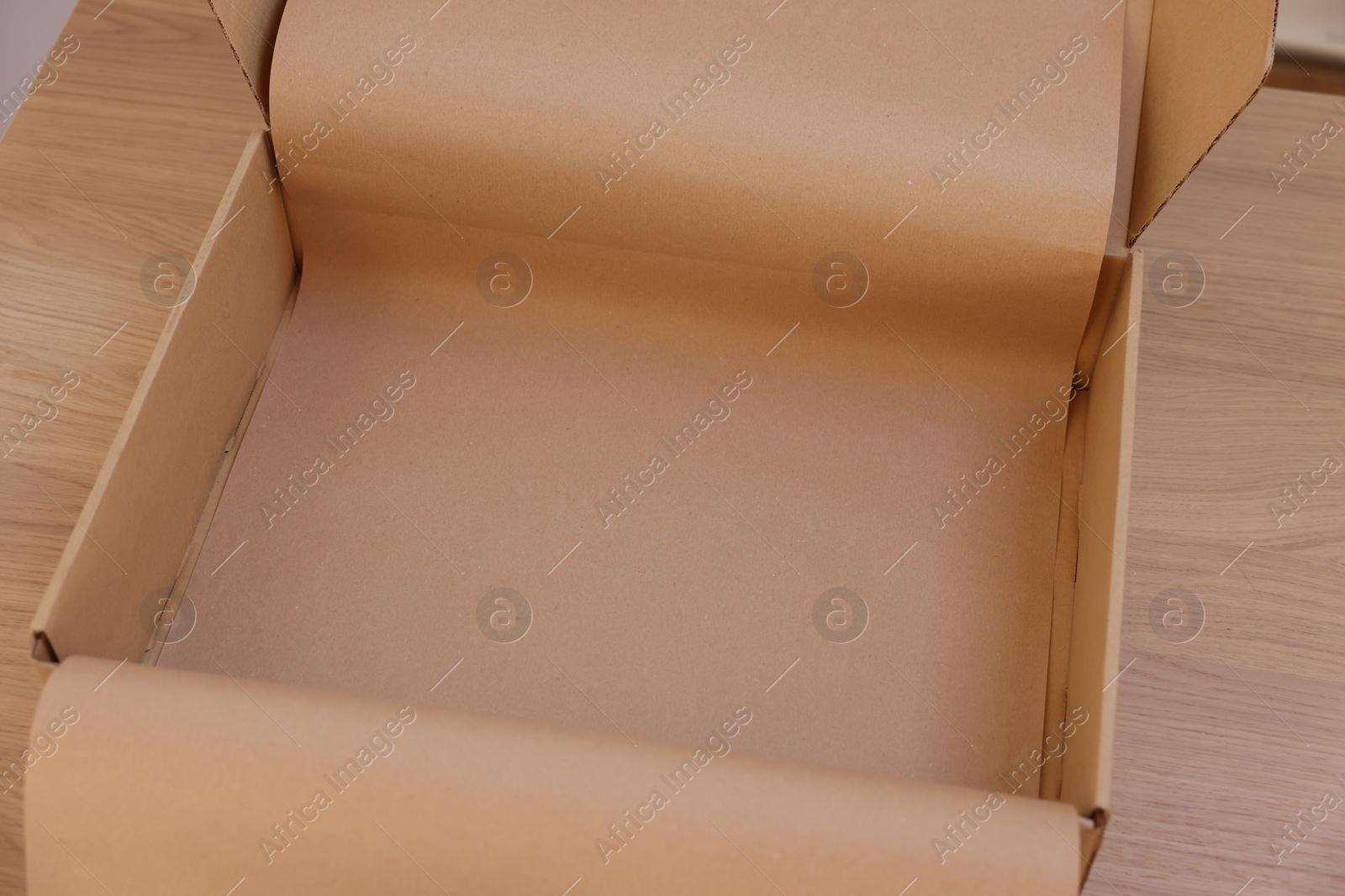 Photo of Empty cardboard box with kraft paper on wooden table. Delivery service