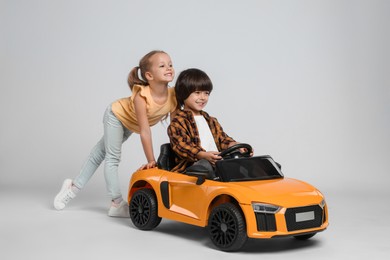 Photo of Cute girl pushing children's electric toy car with little boy on grey background