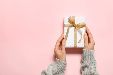 Woman holding Christmas gift on pink background, top view. Space for text