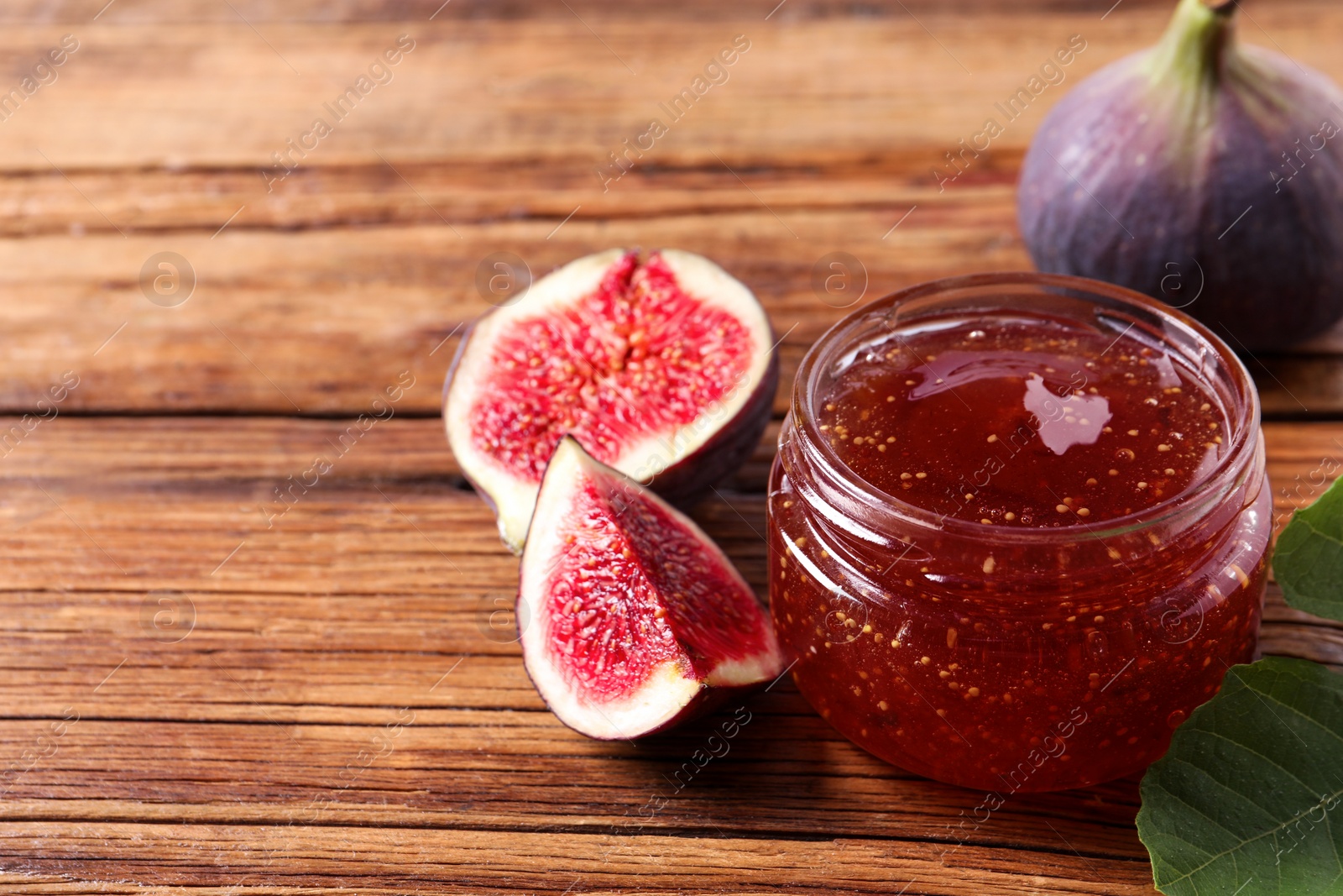 Photo of Jar of tasty sweet jam and fresh figs on wooden table, closeup. Space for text