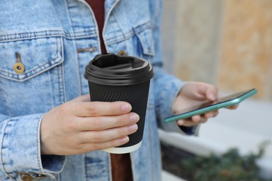 Woman with paper cup of coffee and smartphone outdoors, closeup