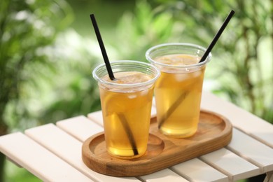 Photo of Plastic cups of tasty iced tea with lemon on white wooden table against blurred background