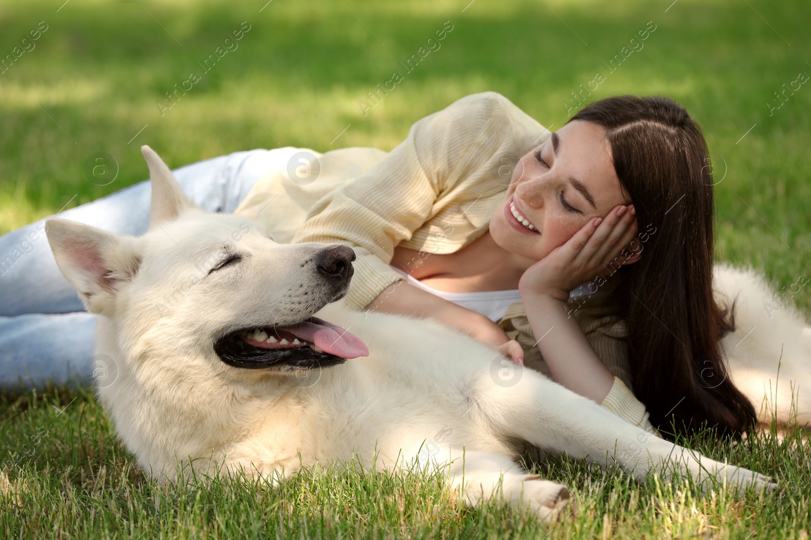 Photo of Teenage girl lying with her white Swiss Shepherd dog on green grass in park