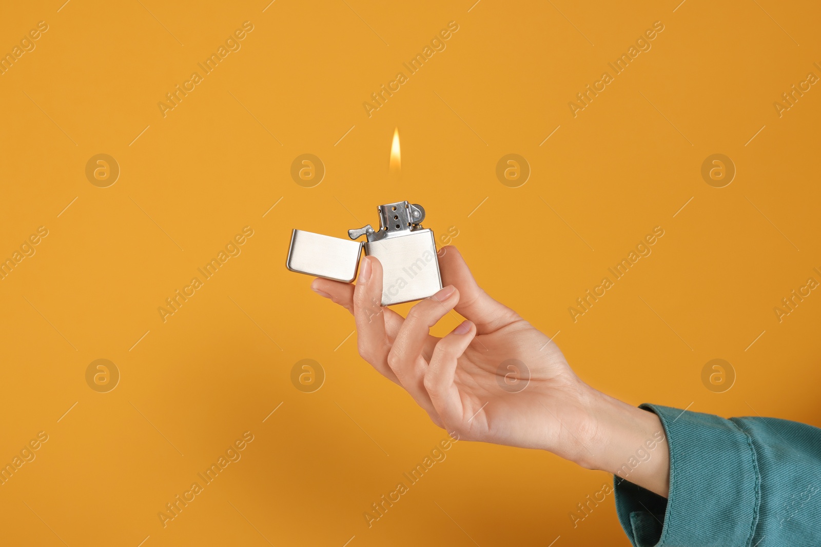 Photo of Woman holding lighter with burning flame on orange background, closeup