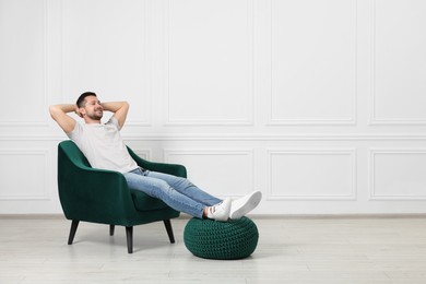 Happy man sitting in armchair indoors, space for text