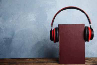 Photo of Book and modern headphones on wooden table. Space for text