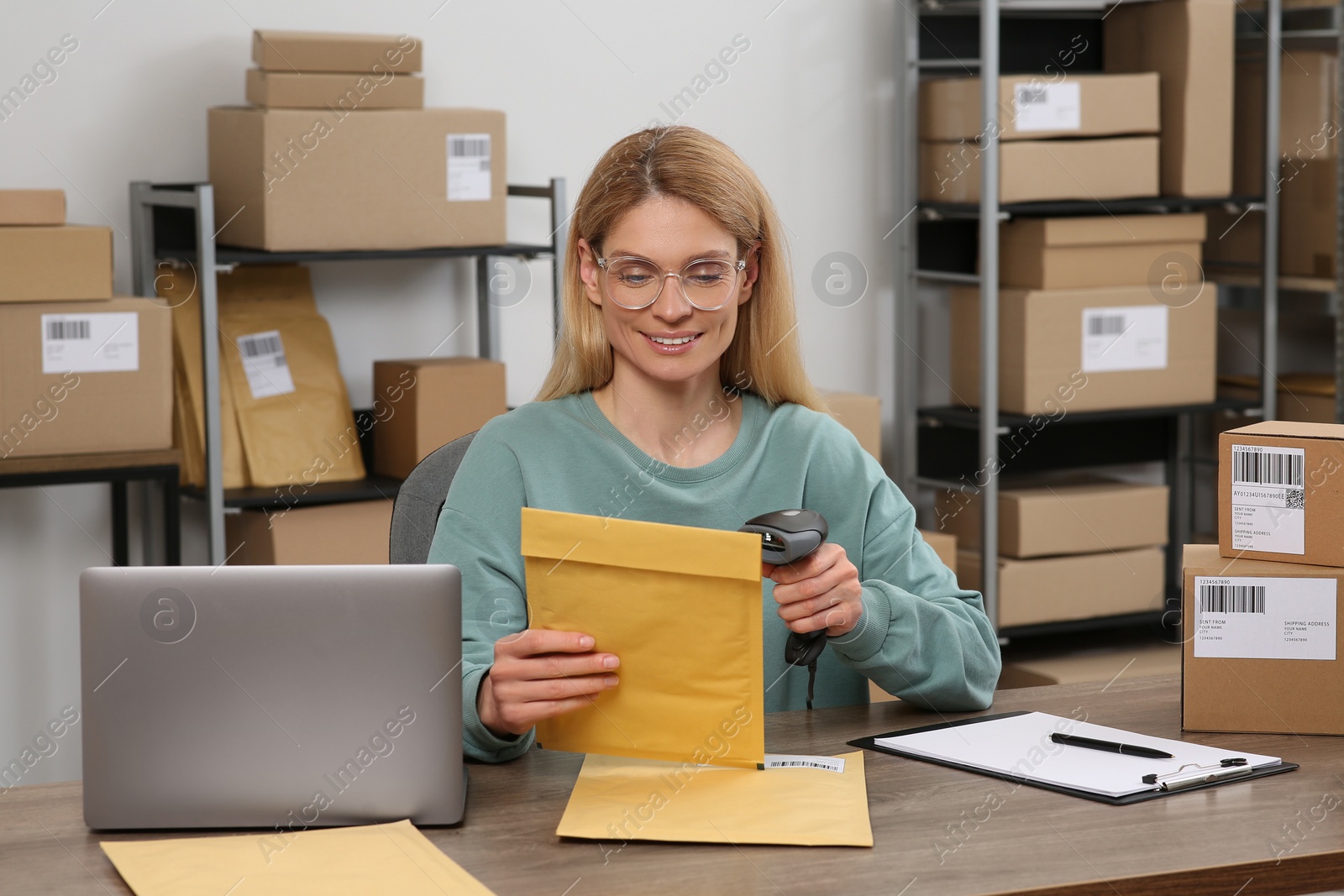 Photo of Seller with scanner reading parcel barcode at table in office. Online store