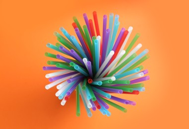 Colorful plastic straws for drinks on orange background, top view