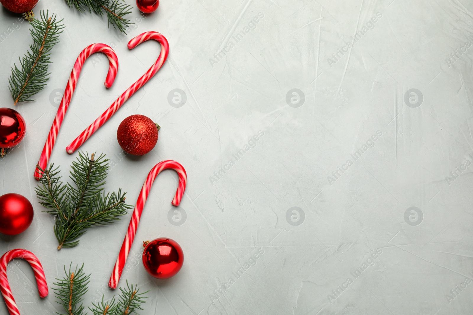 Photo of Tasty candy canes, fir branches and Christmas decor on grey table, flat lay. Space for text