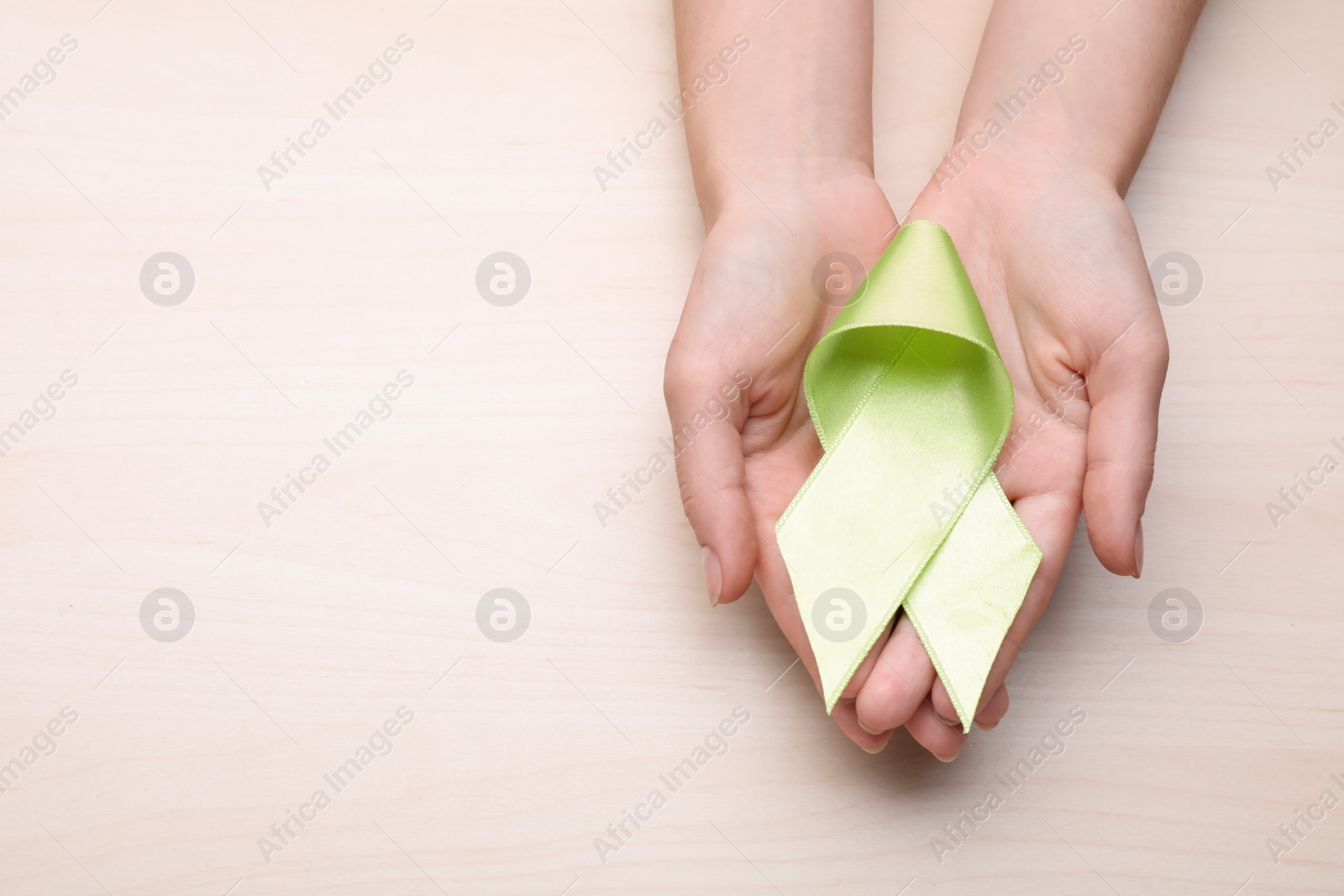 Photo of World Mental Health Day. Woman holding green ribbon on wooden background, top view with space for text