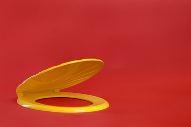 Photo of New yellow plastic toilet seat on red background, space for text