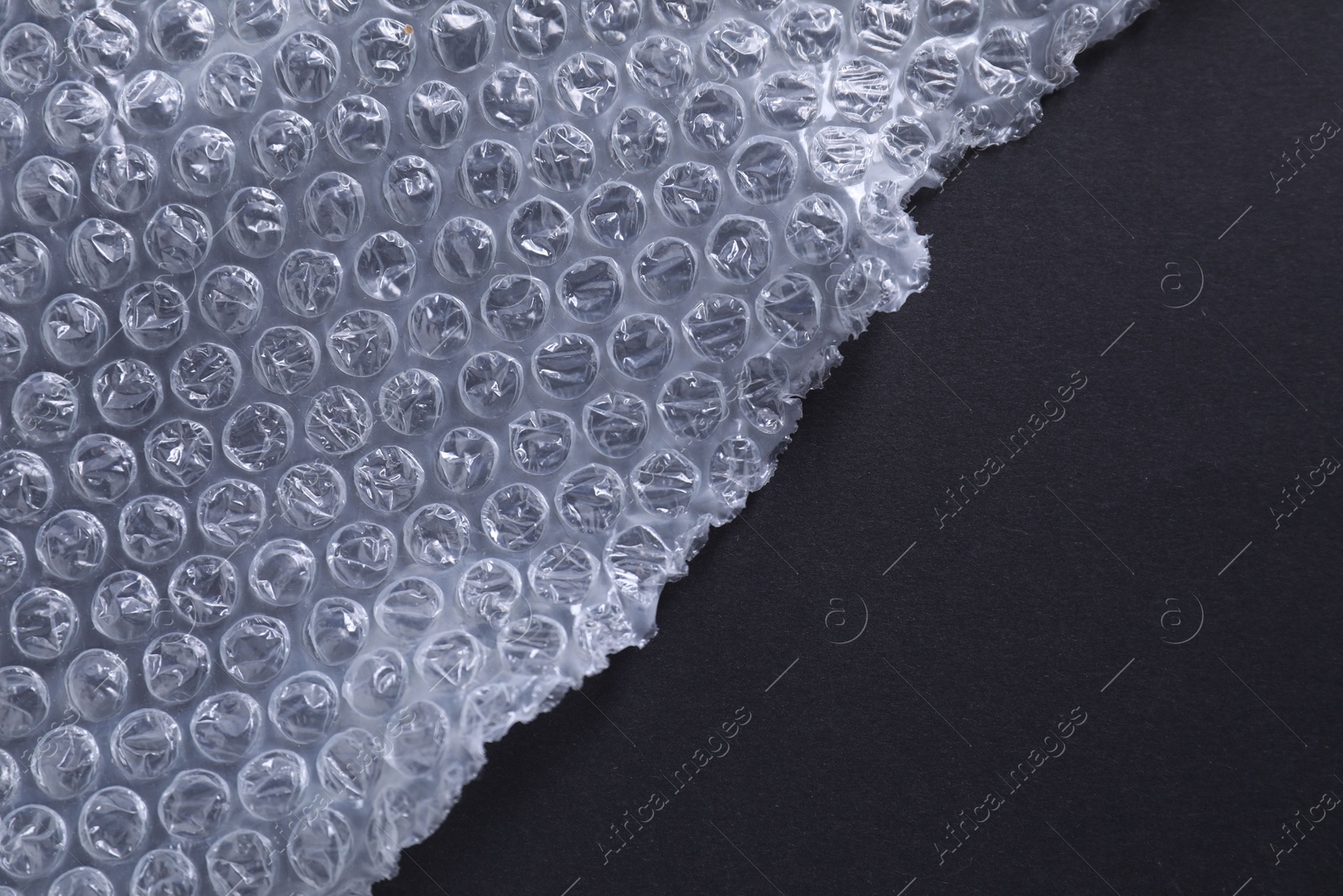 Photo of Transparent bubble wrap on black background, top view. Space for text