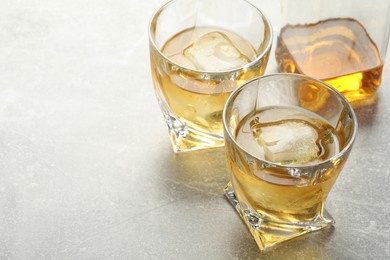 Photo of Tasty whiskey with ice in glasses on light table, closeup. Space for text