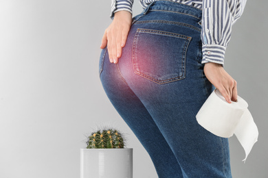 Image of Woman with toilet paper sitting down on cactus against light grey background, closeup. Hemorrhoid concept