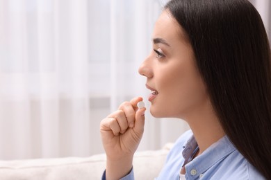 Photo of Beautiful young woman taking pill at home, space for text
