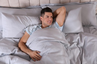 Photo of Man lying in comfortable bed with light grey striped linens, above view