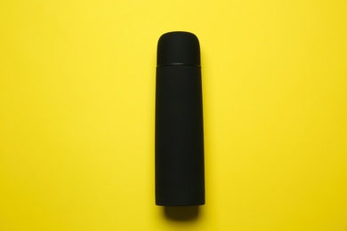 Photo of Black thermos on yellow background, top view
