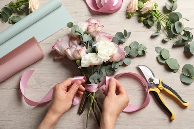 Florist creating beautiful bouquet at wooden table, top view