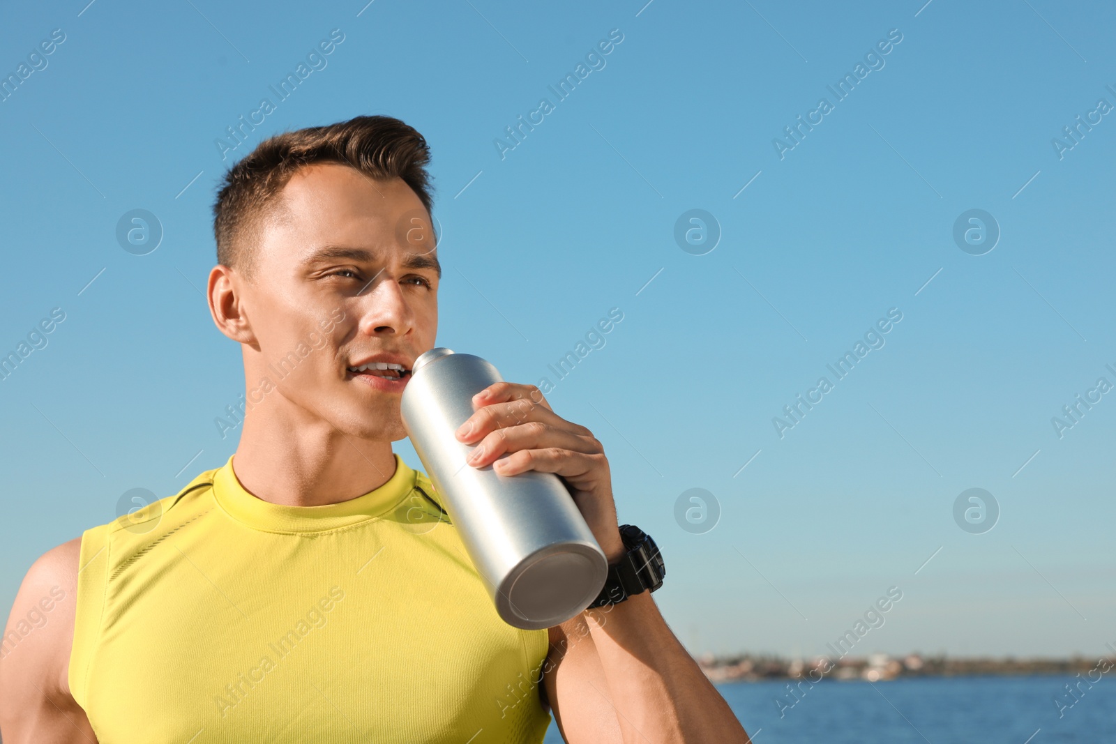 Photo of Young sporty man drinking from water bottle outdoors on sunny day. Space for text