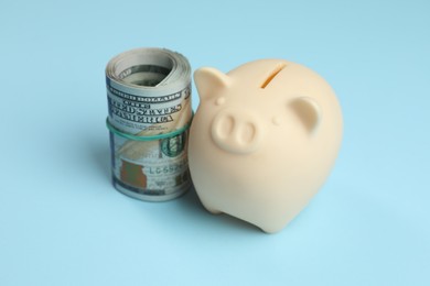 Photo of Money exchange. Rolled dollar banknotes and piggy bank on light blue background