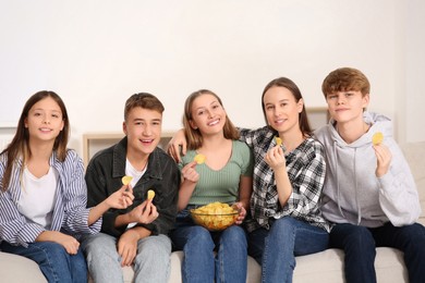 Group of happy teenagers eating chips in room at home