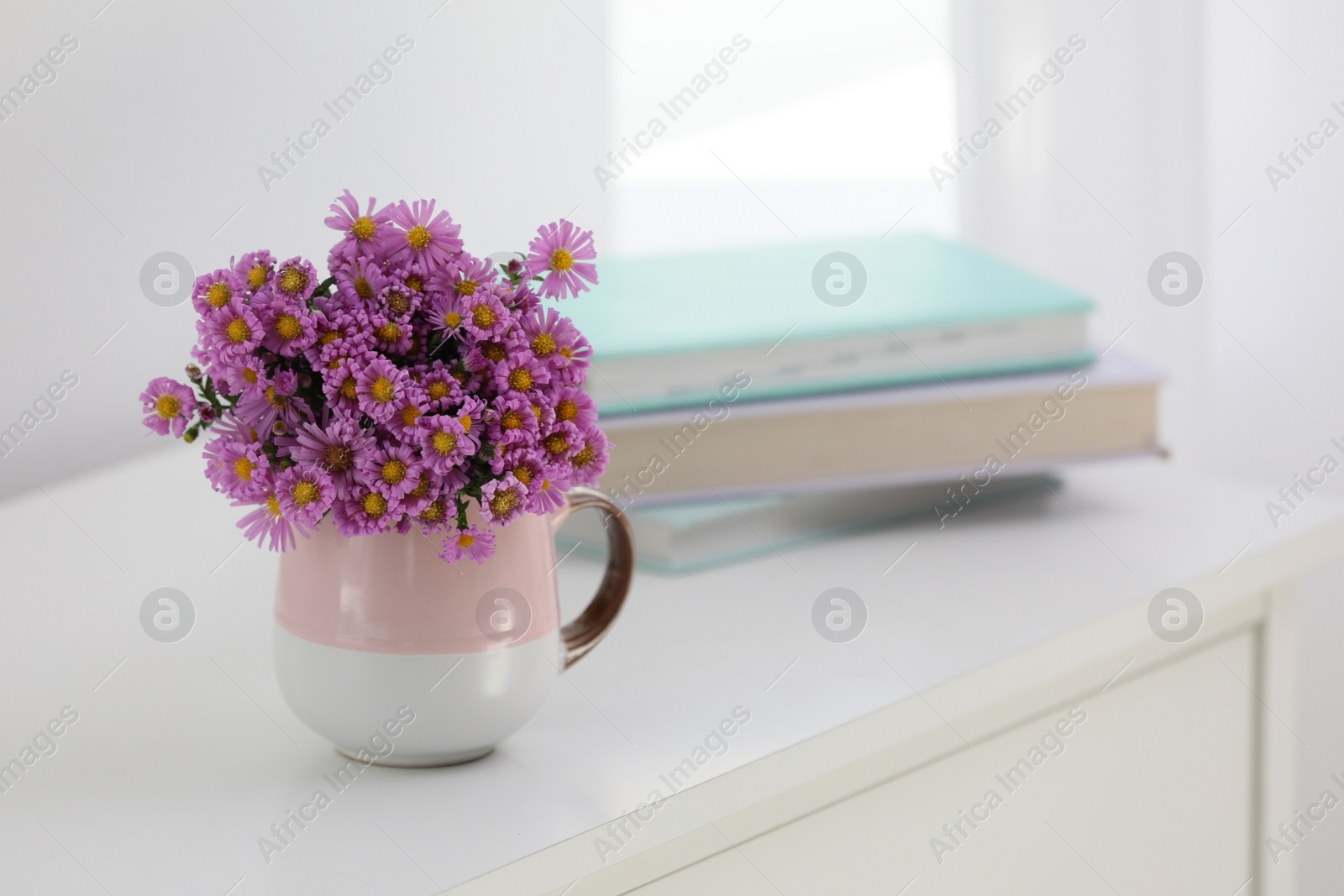 Photo of Cup with beautiful flowers on white table in light room. Space for text