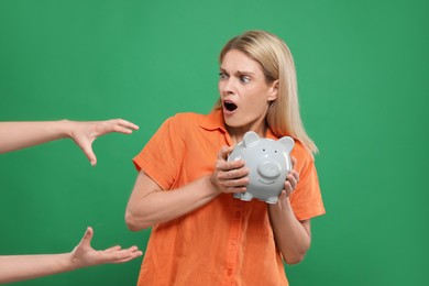Photo of Scammer taking piggy bank from emotional woman on green background. Be careful - fraud
