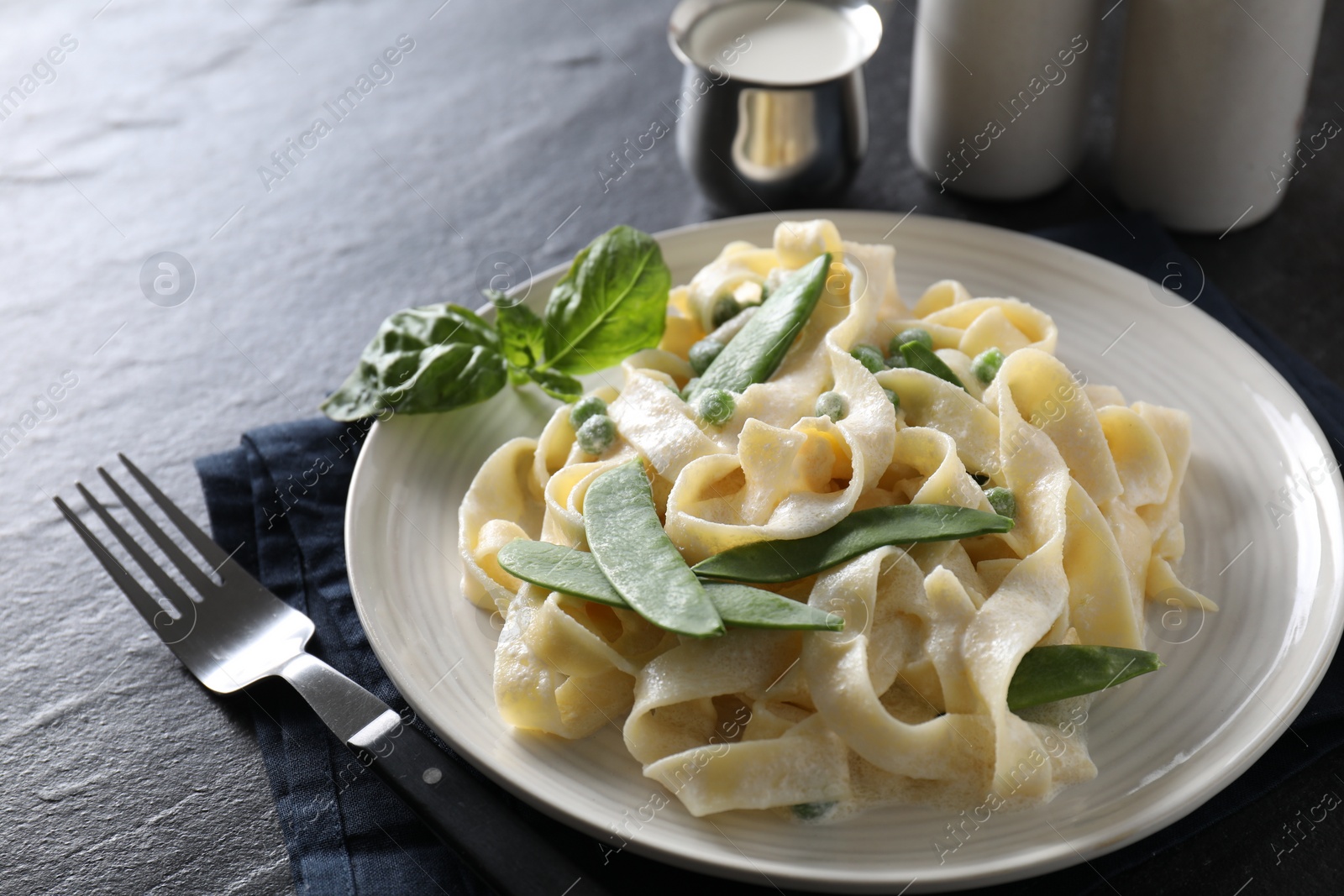 Photo of Delicious pasta with green peas and creamy sauce on black table