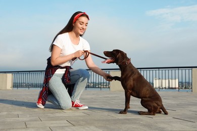 Photo of Young woman with her German Shorthaired Pointer dog on city street