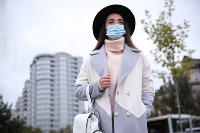 Photo of Young woman in medical face mask walking outdoors. Personal protection during COVID-19 pandemic
