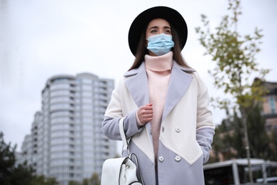 Young woman in medical face mask walking outdoors. Personal protection during COVID-19 pandemic