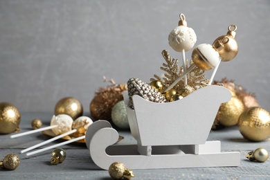 Photo of Delicious Christmas themed cake pops and festive decor on wooden table against grey background