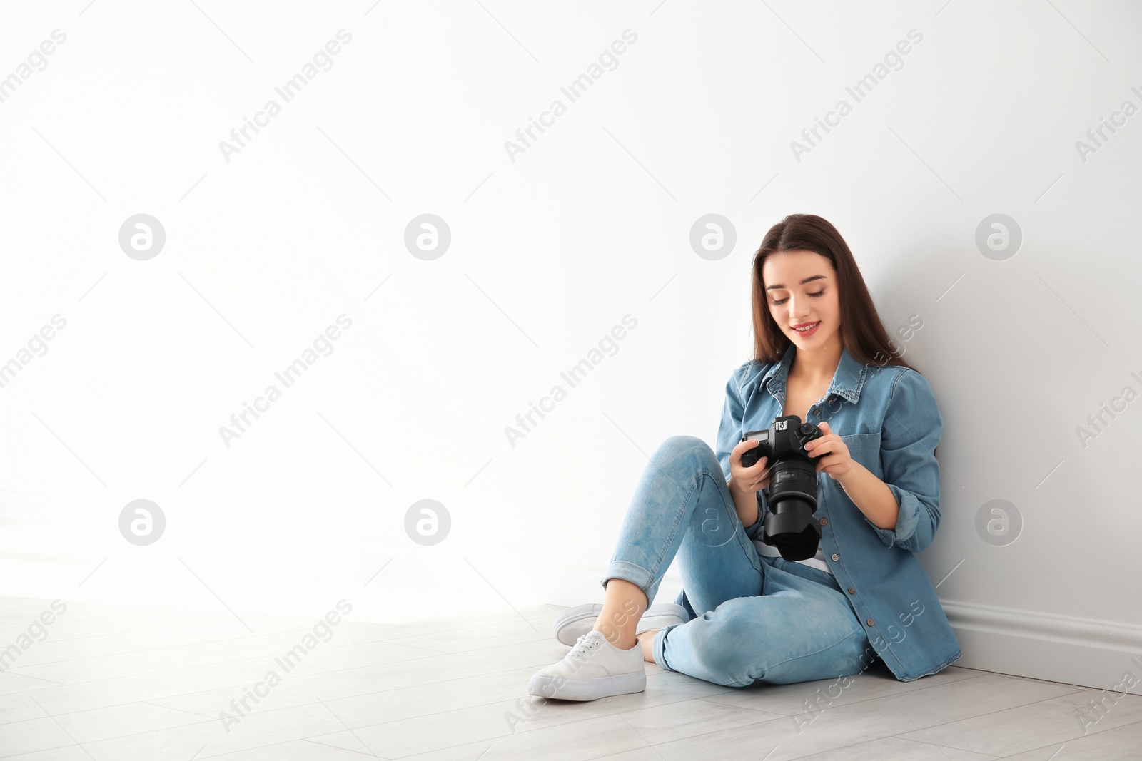 Photo of Female photographer with camera sitting on floor near wall indoors