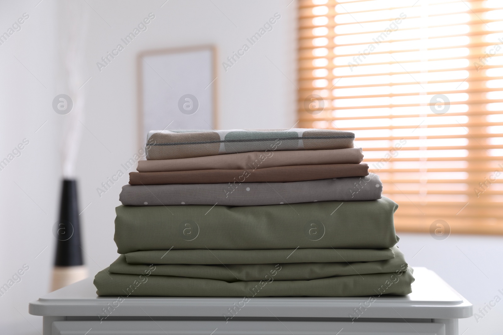 Photo of New clean folded bed linens on table indoors