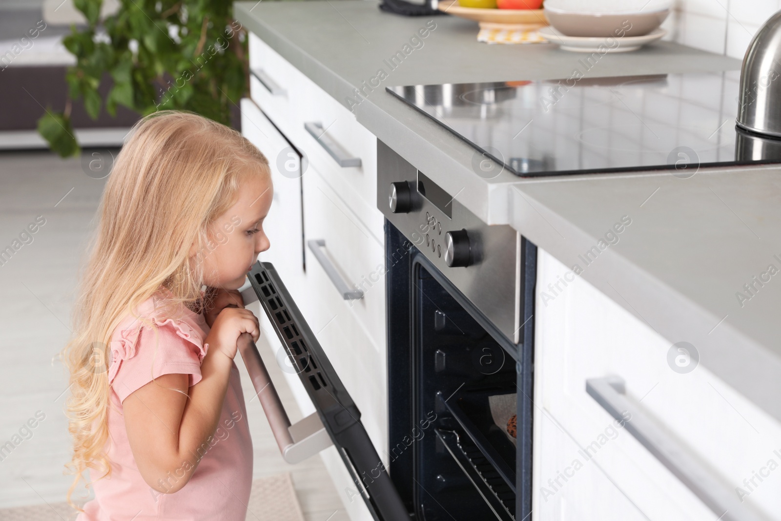 Photo of Little girl baking cookies in oven at home