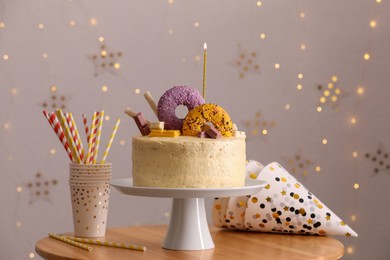 Delicious cake decorated with sweets and burning candle on wooden table