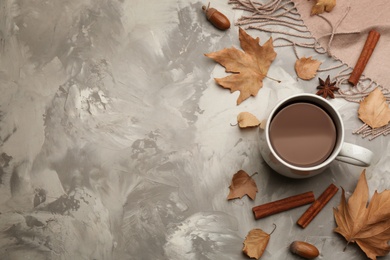 Flat lay composition with cup of hot drink and autumn leaves on grey table, space for text. Cozy atmosphere