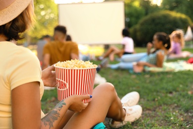 Photo of Young woman with popcorn watching movie in open air cinema, closeup. Space for text