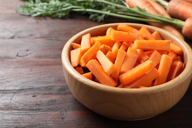 Cut carrot in bowl on brown wooden table, closeup