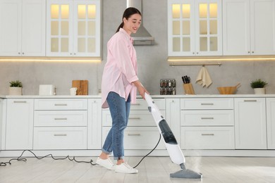 Photo of Happy woman cleaning floor with steam mop in kitchen at home
