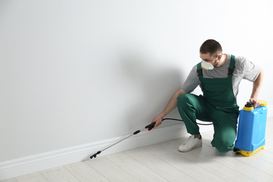 Pest control worker in uniform spraying pesticide indoors. Space for text