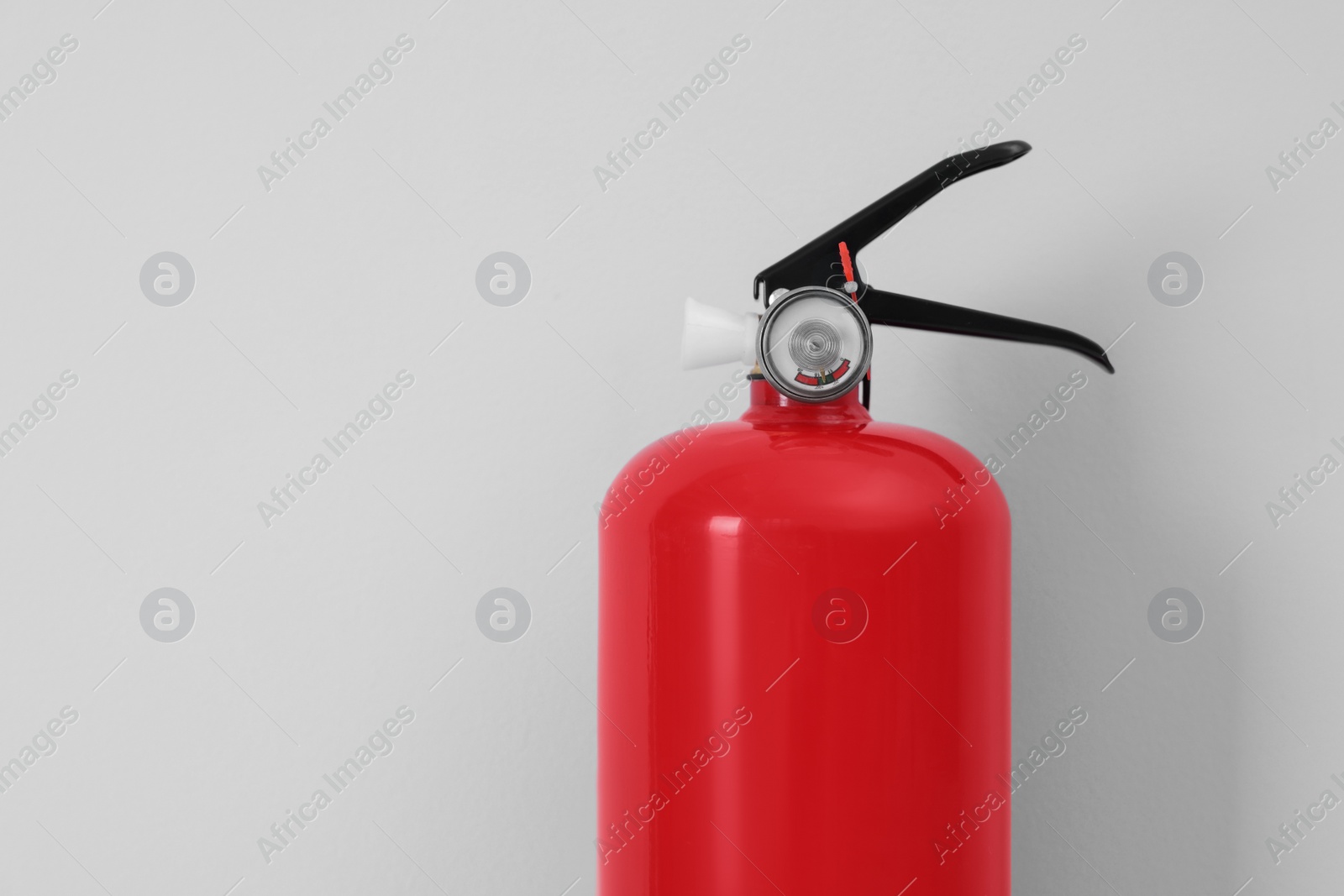 Photo of Fire extinguisher near light grey wall, space for text