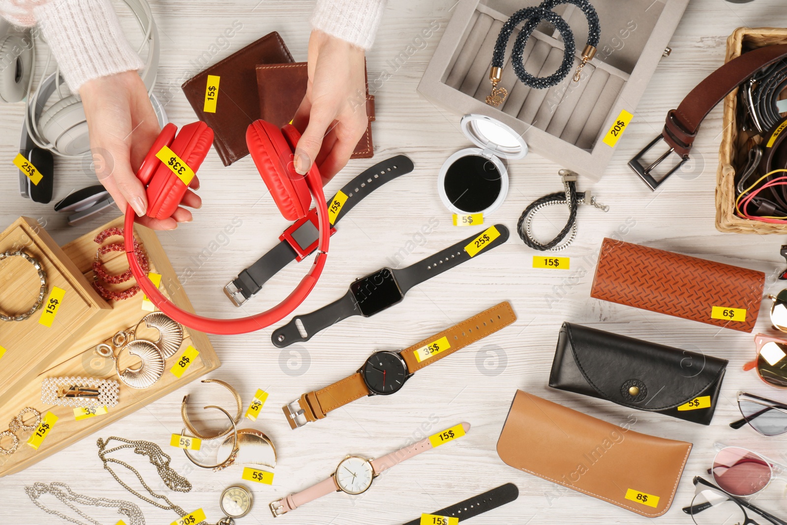 Photo of Woman holding headphones near table with different stuff, top view. Garage sale