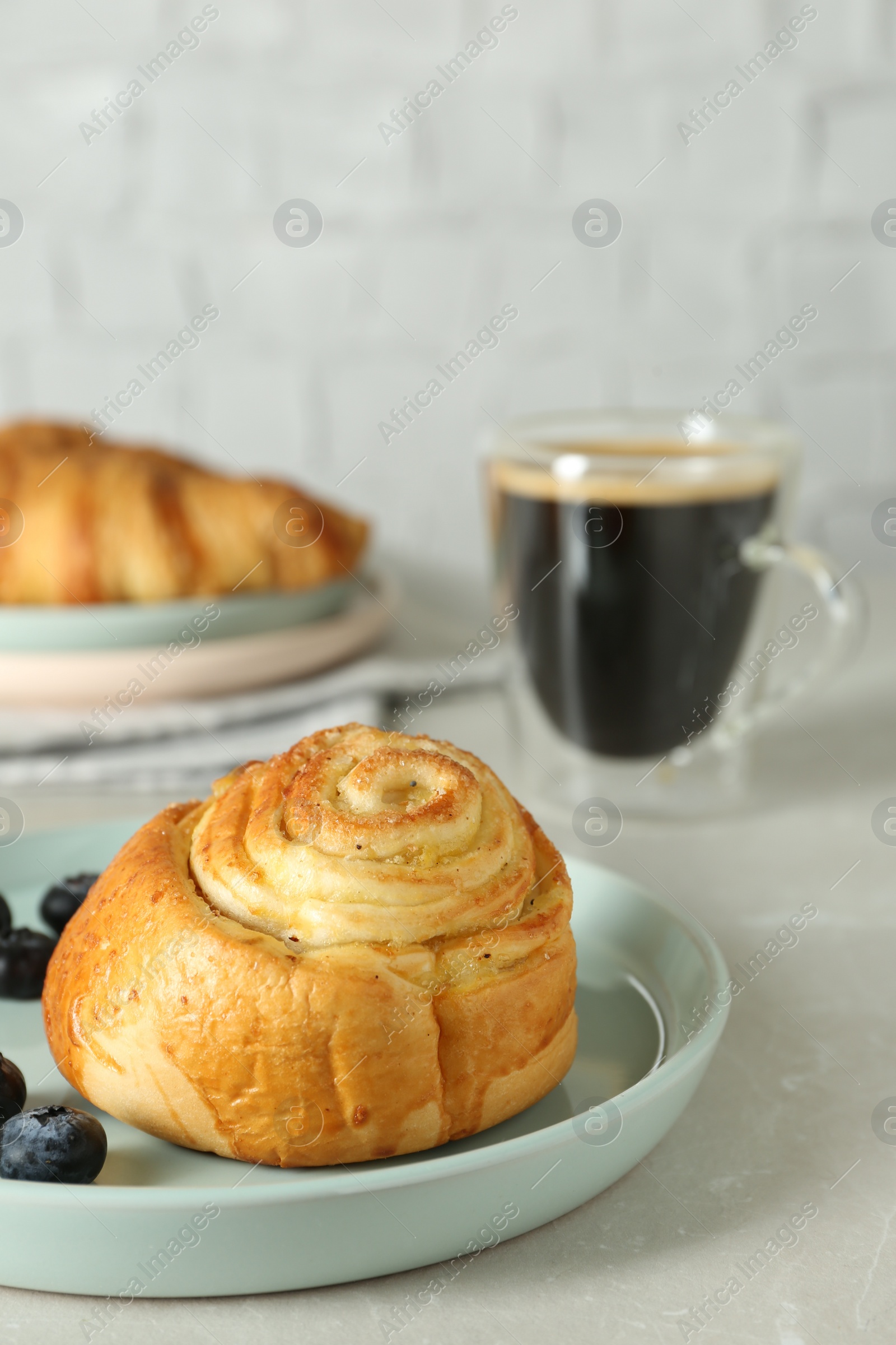 Photo of Delicious bun with blueberries and coffee on white table, closeup