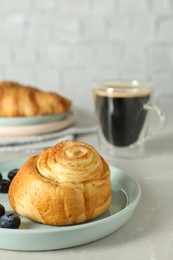 Delicious bun with blueberries and coffee on white table, closeup